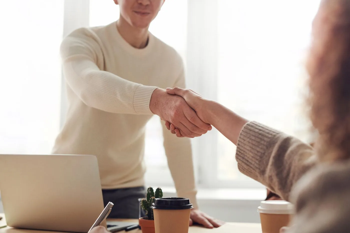 Dos personas cerrando un acuerdo con un saludo de manos sobre una mesa de reunión