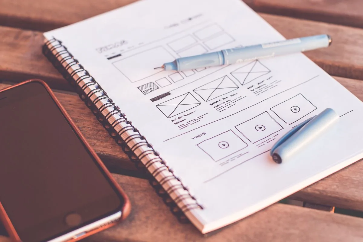 Cuaderno con bocetos de wireframes de una interfaz junto a un teléfono y lápices