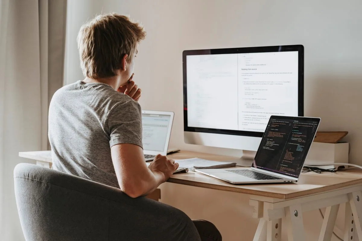 Persona trabajando en un escritorio con un monitor y dos computadores portátiles